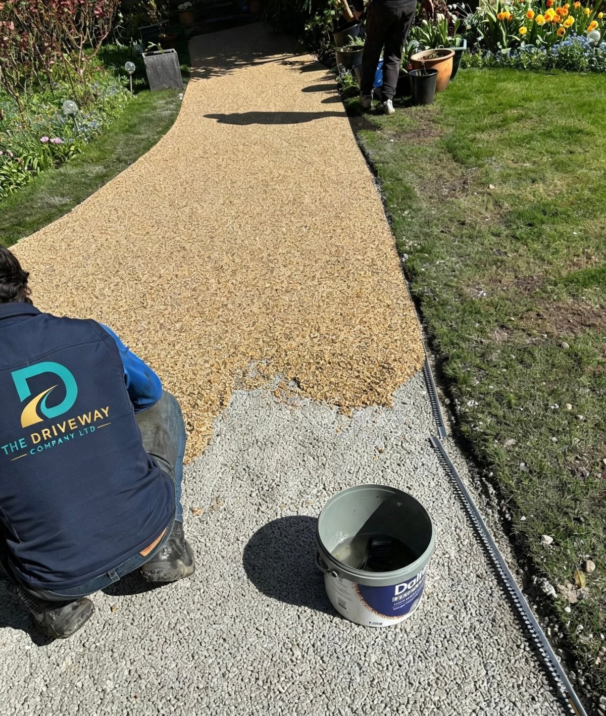 The Driveway Company Ltd team member installing resin bound gravel pathway with company logo visible on branded workwear